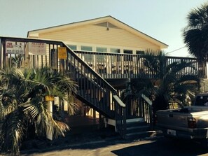 A two-story building with a balcony, palm trees, and a truck parked in front. - Unique Beach Cottage with pool and easy beach access (Gulf Shores)