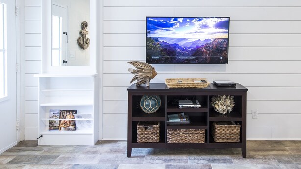 Ein Wohnzimmer mit Fernseher an der Wand, einer weißen Tür und einer dunklen Holzkonsole mit Körben und Dekoration.