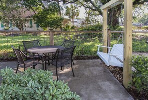 Une terrasse avec une table ronde et des chaises, une balançoire et une pergola en bois.