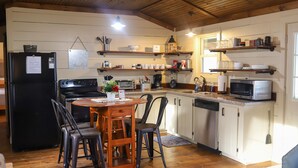 Een keuken met houten kastjes, een koelkast, een magnetron en een eettafel met stoelen.