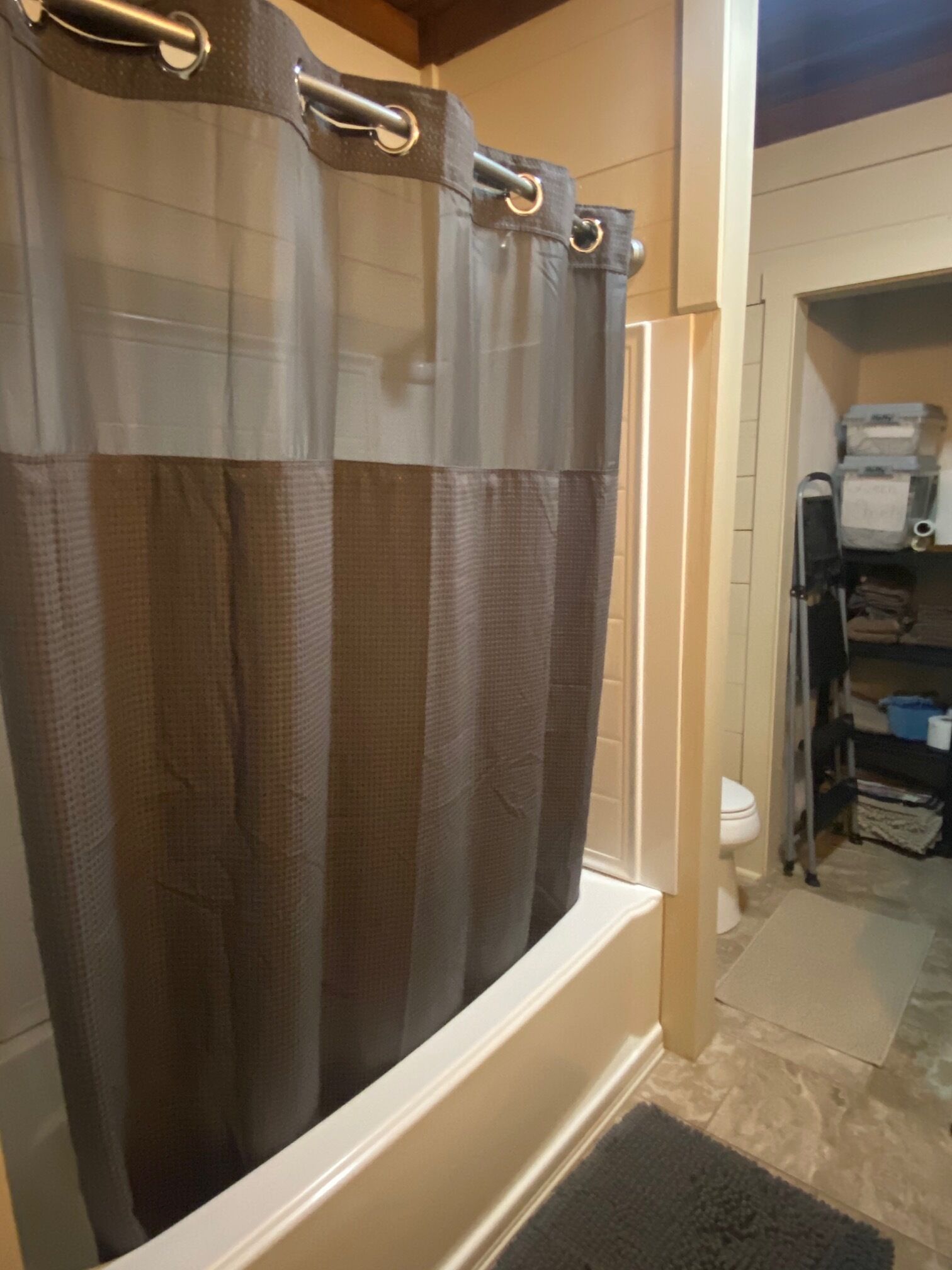 Un baño con cortina de ducha, un inodoro y un área de almacenamiento con estantes.