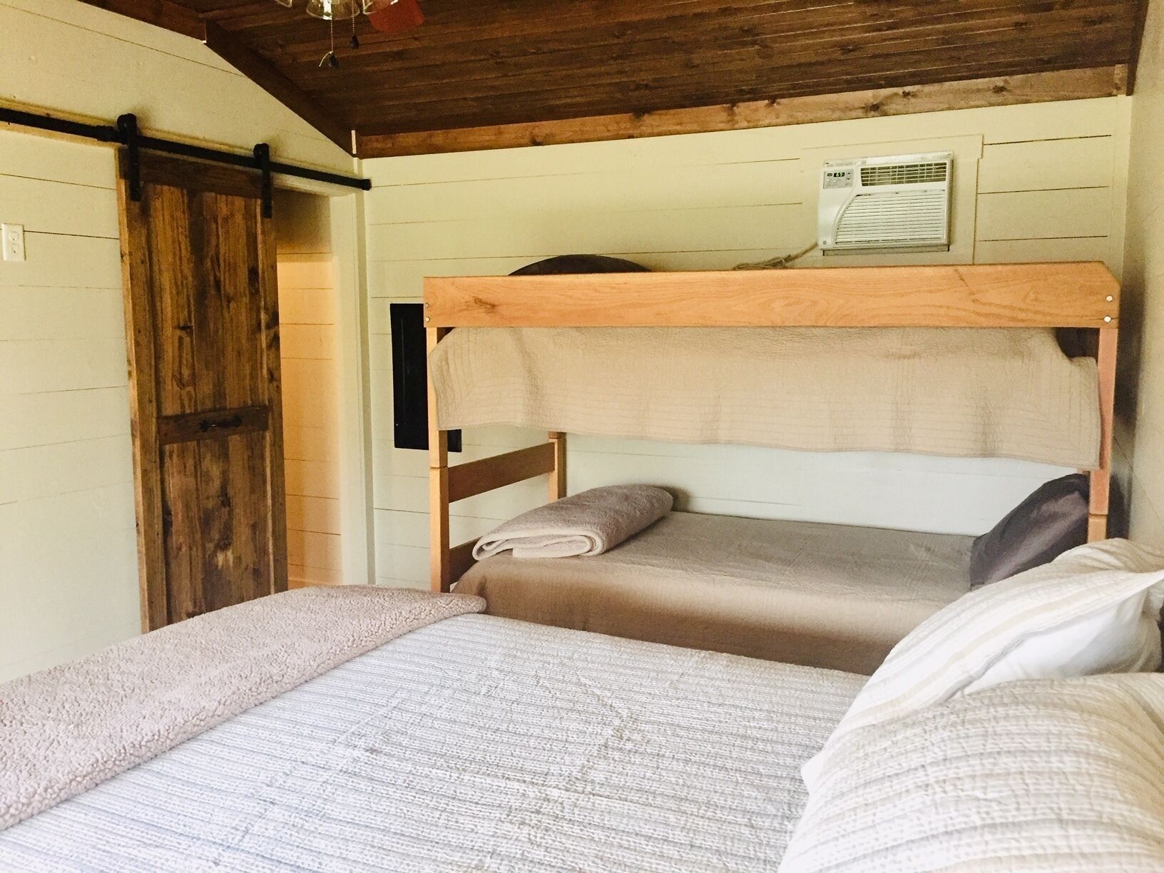 Een slaapkamer met stapelbedden, een houten plafond en een witte muur.