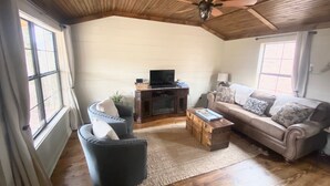 Een woonkamer met een houten plafond, een televisie op een houten kast, een bank, een fauteuil en een salontafel.