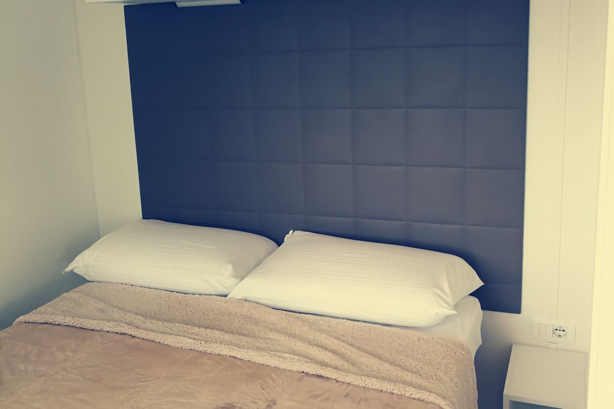 Un dormitorio con cama, cabecera, armario y mesita de noche.