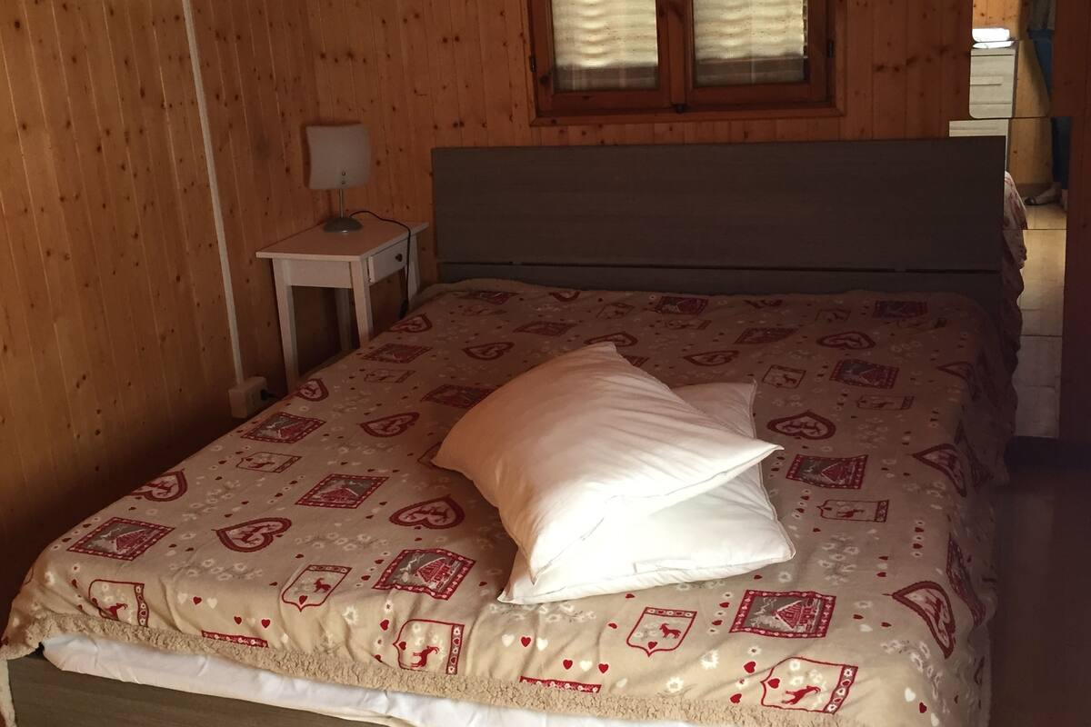 Un dormitorio con cama, mesita de noche, lámpara y ventana con persianas.