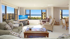 A spacious living room with a large TV, comfortable seating, and a balcony with a view of the beach. - Gulf & Bay Club, TopFloor End Unit 1947sqft incl Lanai, (Siesta Key)