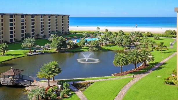 A resort with a pool, palm trees, a beach, and a large building. - Gulf & Bay Club, TopFloor End Unit 1947sqft incl Lanai, (Siesta Key)