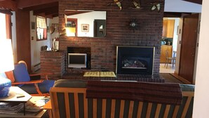 A living room with a brick fireplace, a television, and a sofa. - Authentic Mid-Century Marvel, in the quiet and desirable Mid Town neighborhood. (Bend)