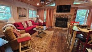 A cozy living room with a fireplace, red sofa, wooden floors, and large windows.