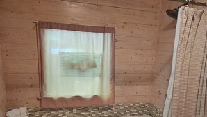 A wooden cabin bathroom with a bathtub, a window with a curtain, and a small table with towels.