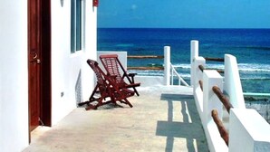 A white building with a door and windows, a wooden chair, and a railing overlooking the ocean. - Casa Rosa -Beautiful Ocean Front Home - Studio Apartment (Isla Mujeres)
