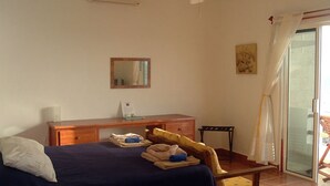 A bedroom with a bed, a wooden dresser, a chair, a mirror, and a sliding glass door to a balcony. - Casa Rosa -Beautiful Ocean Front Home - Studio Apartment (Isla Mujeres)