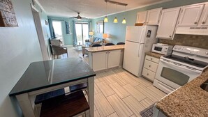 A kitchen with white cabinets, a refrigerator, microwave, and stove. There is a dining area with a table and chairs. - Direct Beachfront OFV D108 Private Beach 2BR 2BA (Myrtle Beach)