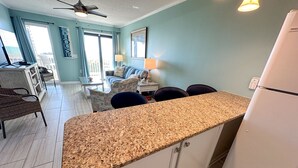 A kitchen with a granite countertop, white cabinets, and a white refrigerator. There is a dining area with a table and chairs, and a living room with a couch and a lamp. - Direct Beachfront OFV D108 Private Beach 2BR 2BA (Myrtle Beach)
