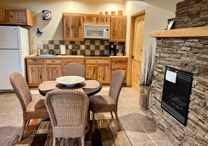 A kitchen with wooden cabinets, a microwave, a stone fireplace, and wicker chairs around a round table.