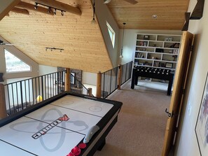 A room with a foosball table, a bookshelf, and a staircase with a wooden railing.