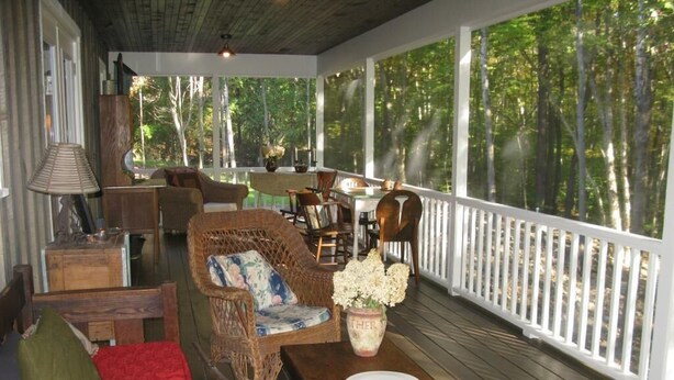 A covered porch with wicker furniture, a dining table, and a view of the forest. - Lovely Cottage That Is Completely New With All The Luxuries You Would Want!   (Great Valley)