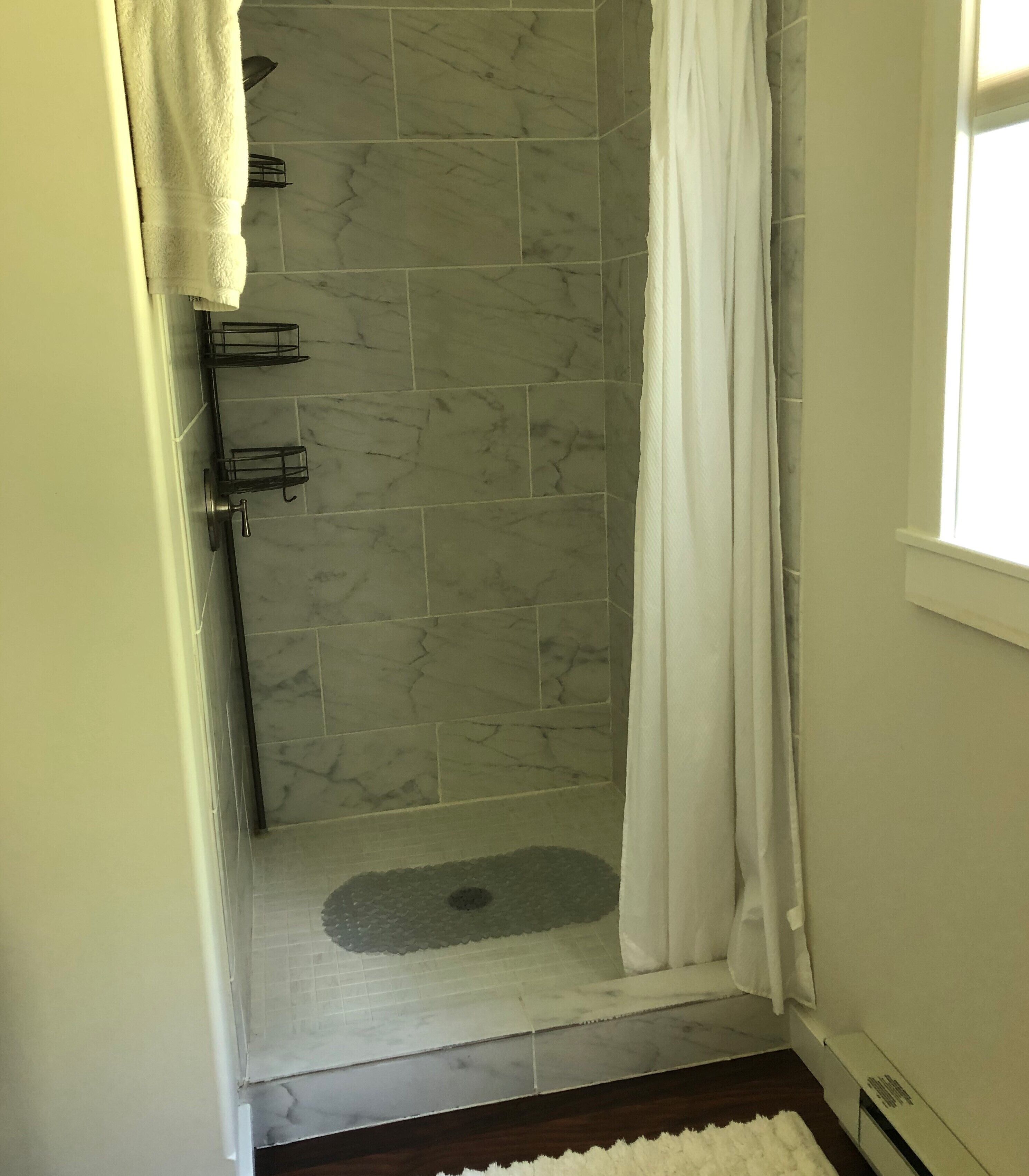 Un área de ducha con puerta de vidrio, una toalla blanca colgada en la pared y un tapete en el suelo.