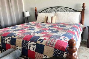 Uma cama com colcha, luminária e cabeceira de madeira.