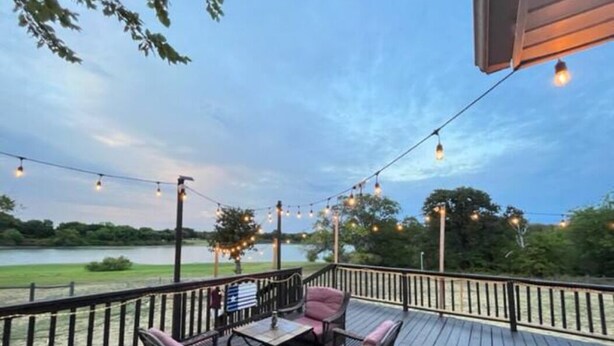 A deck with wicker furniture and string lights, overlooking a body of water. - Beautiful Kayewood Waterfront Retreat (Little Elm)