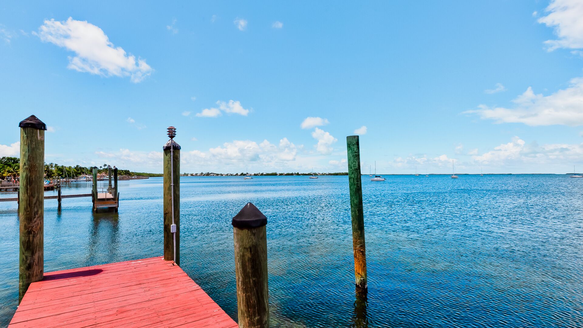 A wooden pier with a red walkway leading into calm blue waters, surrounded by wooden posts and a clear sky.