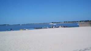 A beach with clear skies, calm water, and a few boats. There are beach chairs and umbrellas along the shore. - Gorgeous Designer Contemporary Beach House with Views (Clinton)