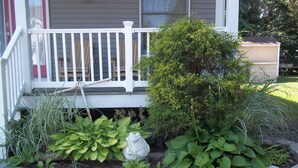A house with a porch, a garden with various plants, and a white fence. - Gorgeous Designer Contemporary Beach House with Views (Clinton)