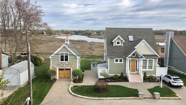 A residential area with two houses, a driveway, and a body of water in the background. - Gorgeous Designer Contemporary Beach House with Views (Clinton)