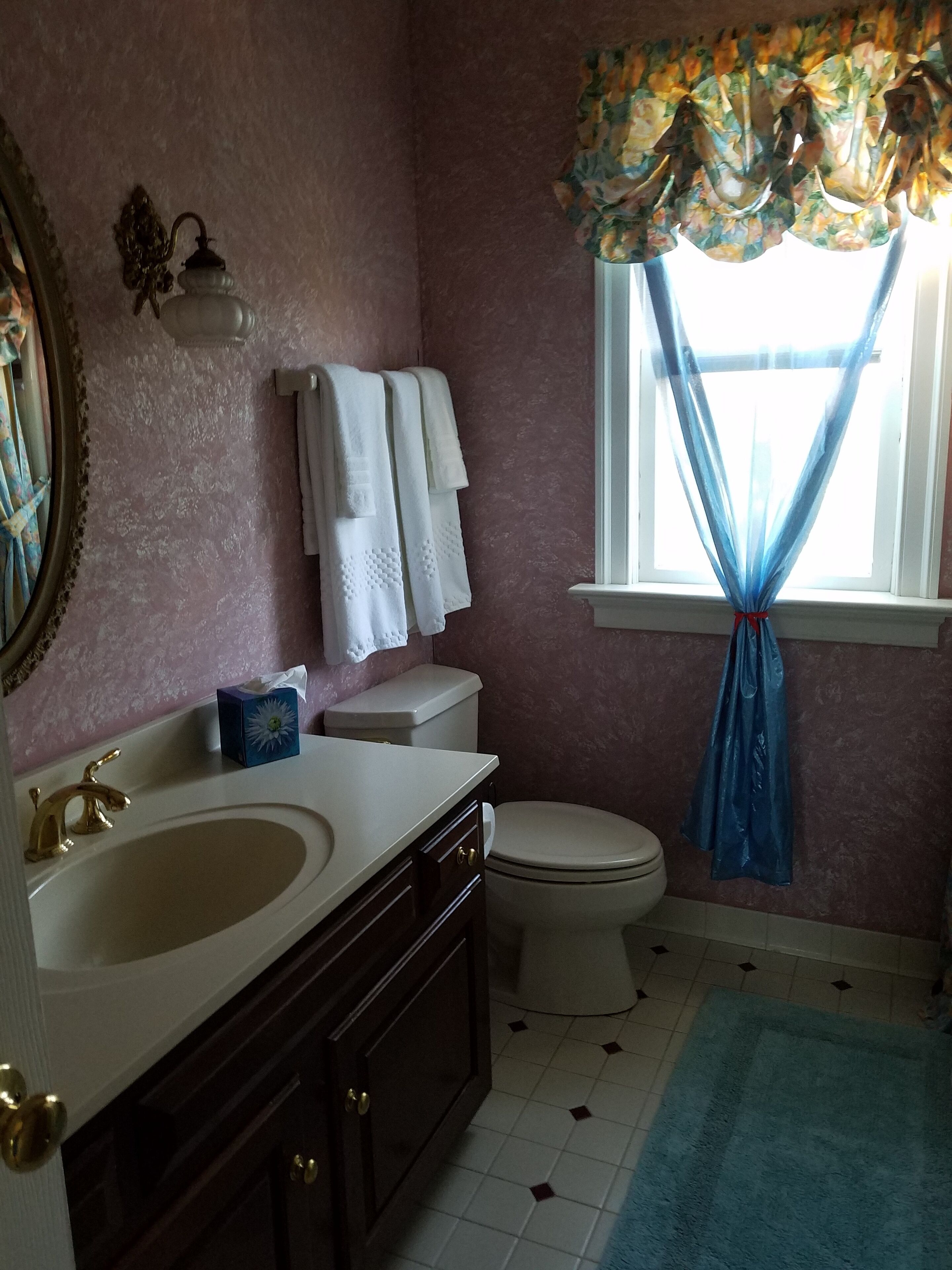 A bathroom with a sink, vanity, toilet, and a window with a curtain.