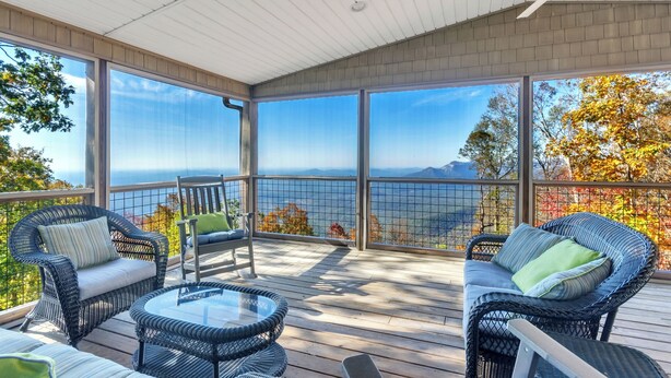 A covered outdoor deck with wicker furniture, a glass table, and a view of the mountains. - Caesar's Head Mountain Home ~ Sleeps 13 ~ Table Rock & Blue Ridge Views (Cleveland)