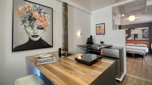 A modern kitchen with a wooden countertop, a refrigerator, and a coffee machine. There is a painting on the wall and a bed in the adjacent room. - PLACE DES ARTS / ART'S PLACE (Ville de Québec)