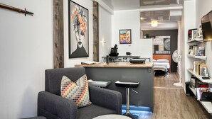 A modern hotel room with a grey sofa, a small bar area, a bed, and a bookshelf. - PLACE DES ARTS / ART'S PLACE (Ville de Québec)