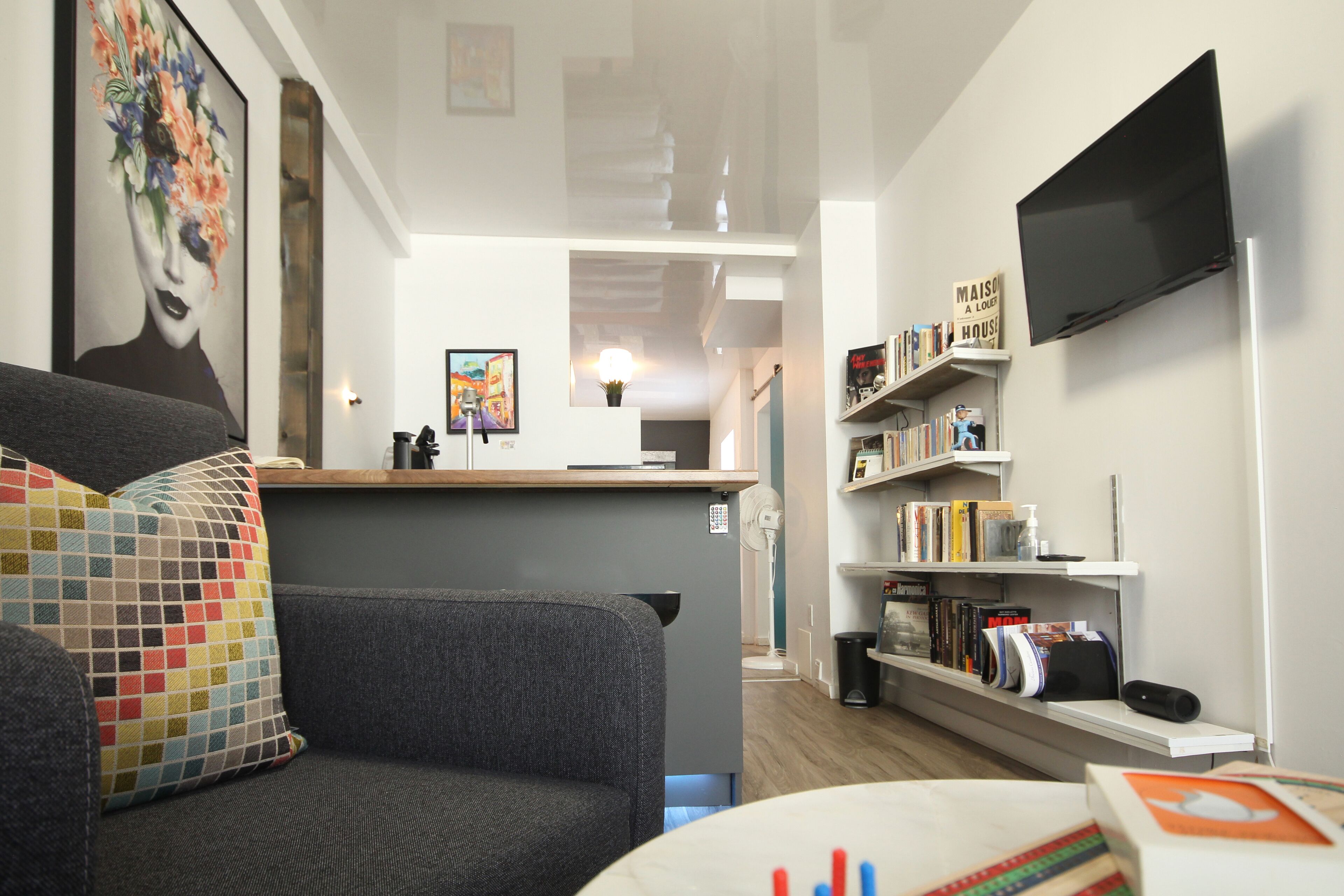 Ein modernes Wohnzimmer mit grauem Sofa, einem Couchtisch, einem Bücherregal und einem an der Wand montierten Flachbildfernseher.