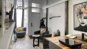 A modern living room with a wooden dining table, grey sofas, and a large floral artwork on the wall. - PLACE DES ARTS / ART'S PLACE (Ville de Québec)