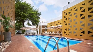 Una piscina con solárium empedrado, tumbonas, sombrillas y una pared decorativa.