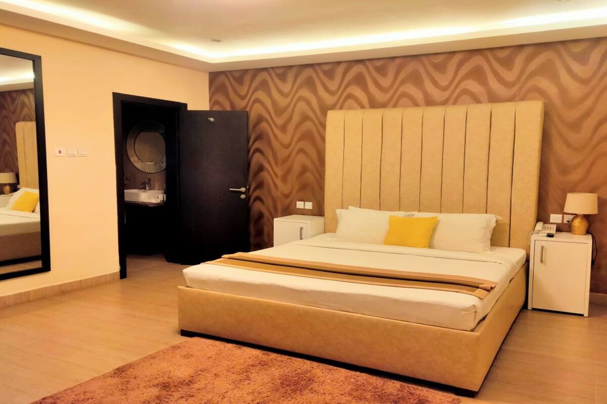 A modern bedroom with a large bed, bedside tables, a mirror, and a wardrobe.