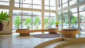 Un vestíbulo amplio con ventanas grandes, asientos de madera y plantas en macetas.