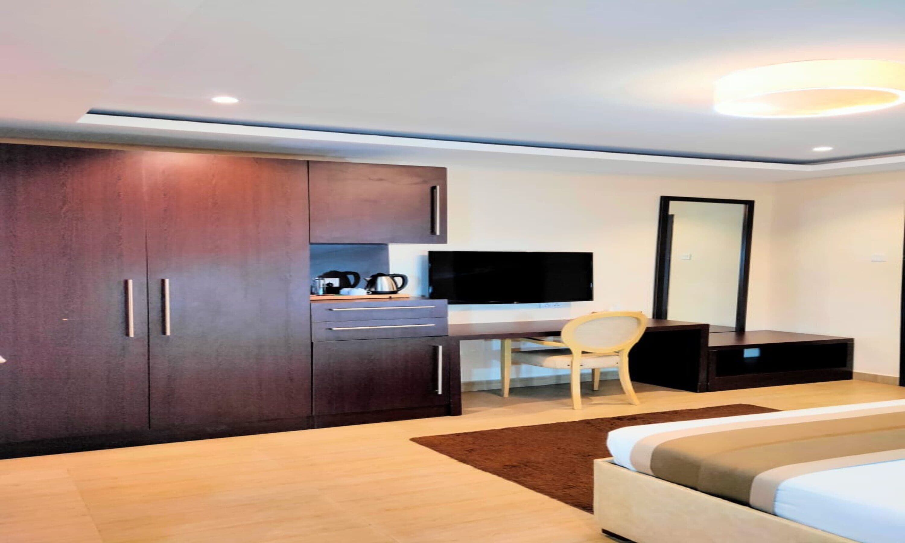 Una habitación de hotel moderna con una cama grande, un escritorio con una silla, un televisor y un armario.