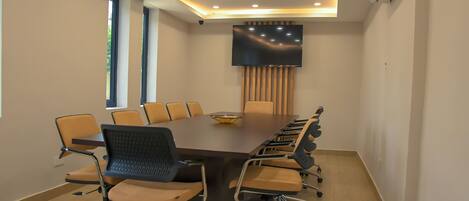 A conference room with a long table, chairs, a flat-screen TV, and a ceiling-mounted air conditioner.