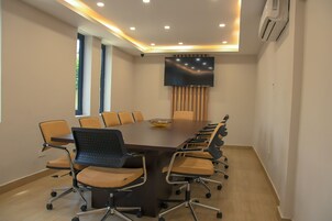 A conference room with a long table, chairs, a flat-screen TV, and a ceiling-mounted air conditioner.