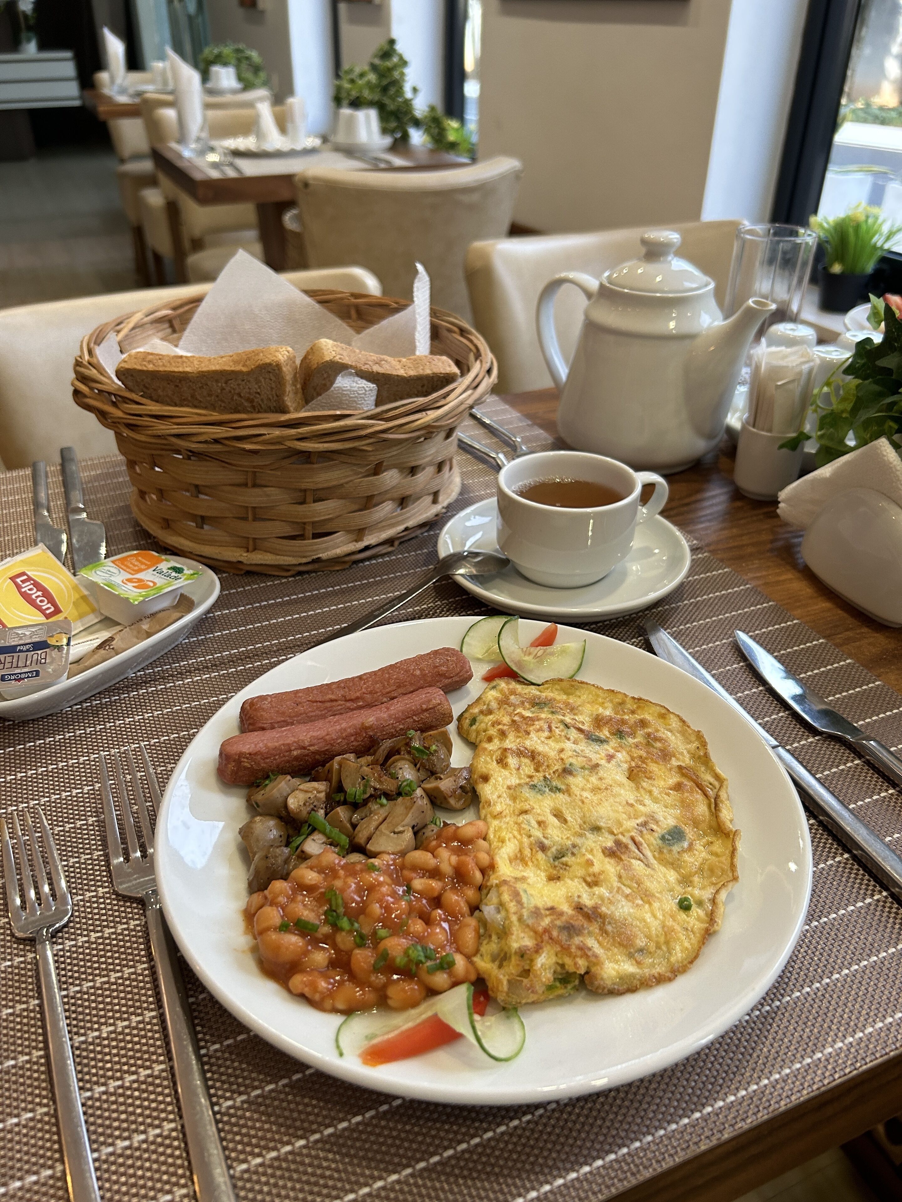 A breakfast setting with a plate of food, a teapot, and a cup of tea.