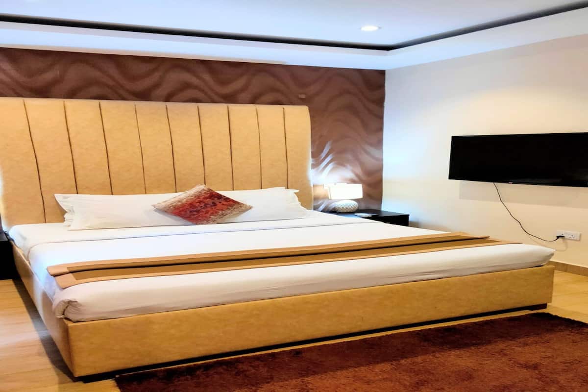 A modern hotel room with a large bed, a flat-screen TV mounted on the wall, and a wooden headboard.