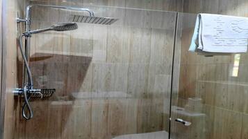 A glass-enclosed shower with a handheld showerhead and a wall-mounted faucet.