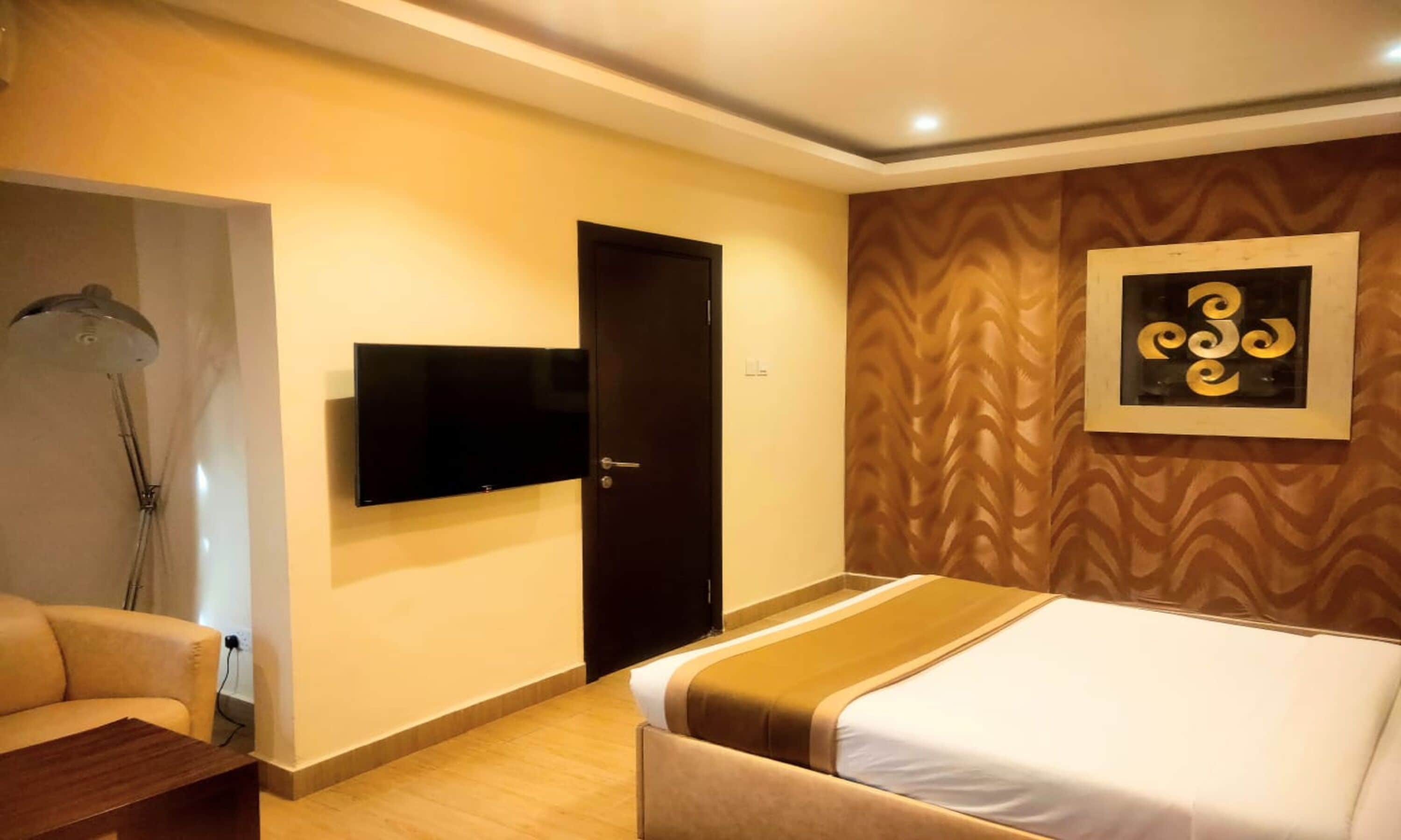 Habitación de hotel con una cama, televisión montada en la pared, una puerta y un papel tapiz estampado.