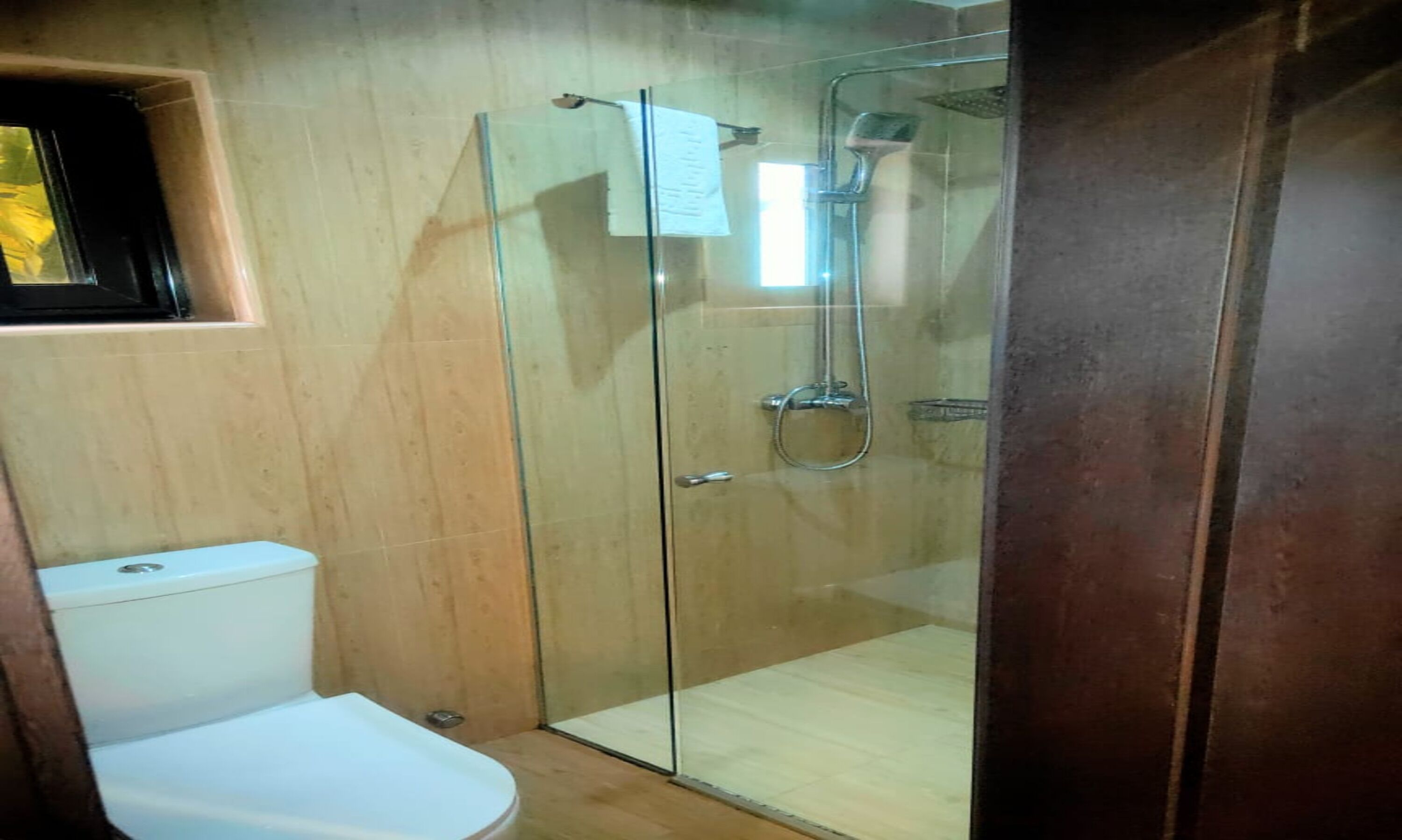 A glass-enclosed shower stall with a toilet and sink in a bathroom with wooden walls.