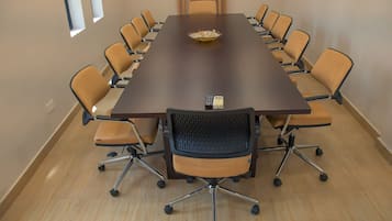 Una sala de conferències amb una taula llarga, diverses cadires i un comandament a la taula.