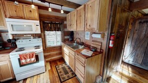 A rustic kitchen with wooden cabinets, a white stove, a microwave, and a sink.