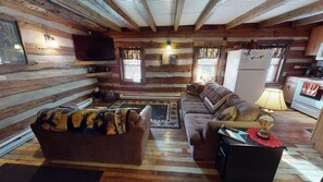 A log cabin interior with a sofa, a television, a refrigerator, and a dining area.