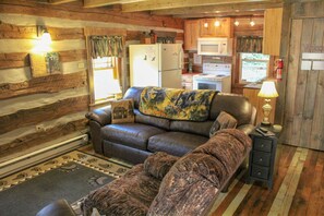 A log cabin interior with a leather sofa, a small table, and a kitchen area.