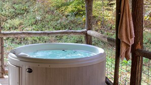 A hot tub in a wooden deck area with a view of a wooded landscape.